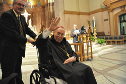 Archbishop Emeritus Daniel M. Buechlein acknowledges the applause given to him from the people gathered at SS. Peter and Paul Cathedral in Indianapolis on Oct. 18 for the press conference at which Archbishop Joseph W. Tobin was introduced as the new shepherd of the Church in central and southern Indiana. Assisting Archbishop Buechlein is Don Mucci, left. Archdiocesan director of communications Greg Otolski, right, joins in the applause. (Photo by Sean Gallagher)